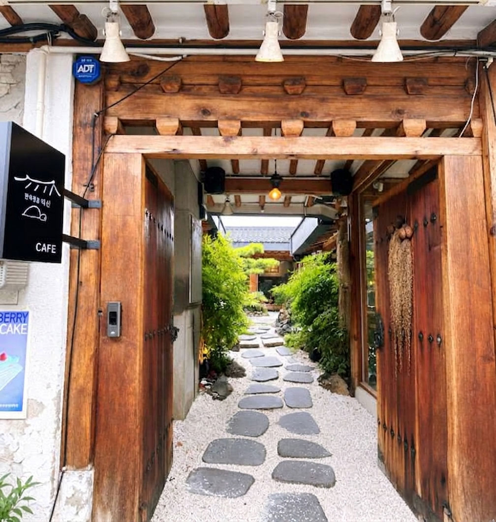 A wooden hanok gateway leading to a green courtyard café in Ikseon-dong